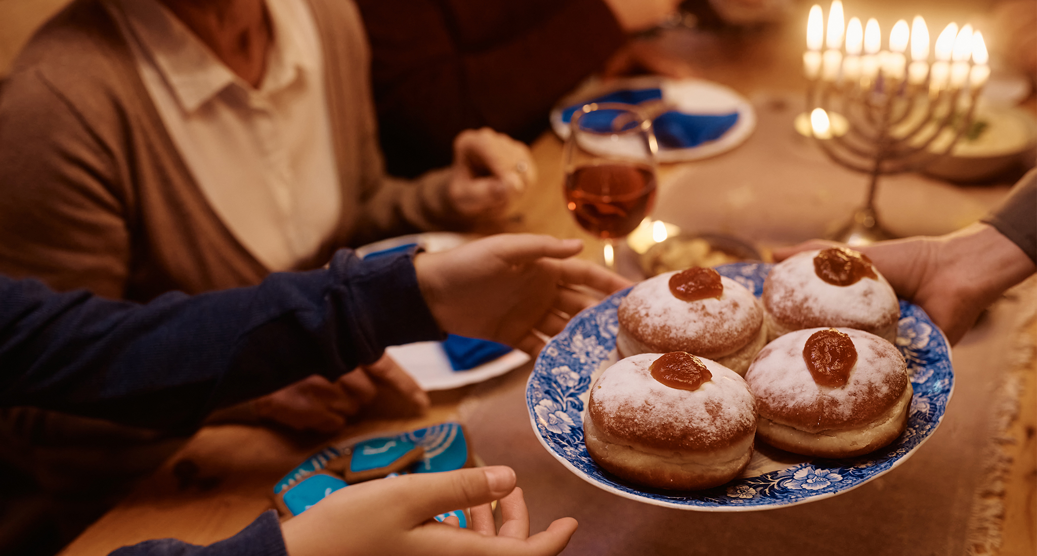 hanukkah-traditions: a family gathered around the table serving a plate of jelly donuts.