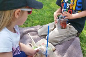 two kids having a slushy treat outside on a picnic blanket