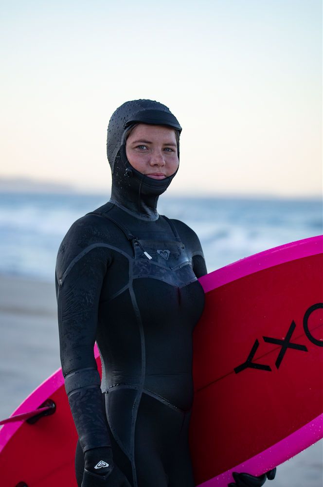 This may contain: a woman in a wet suit holding a surfboard