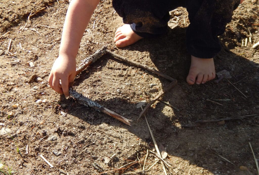 toddler creating a square outside using sticks on the dirt