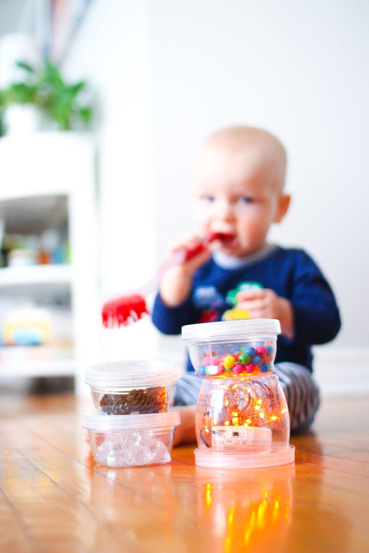 This may contain: a baby sitting on the floor eating food out of plastic containers with candy in them