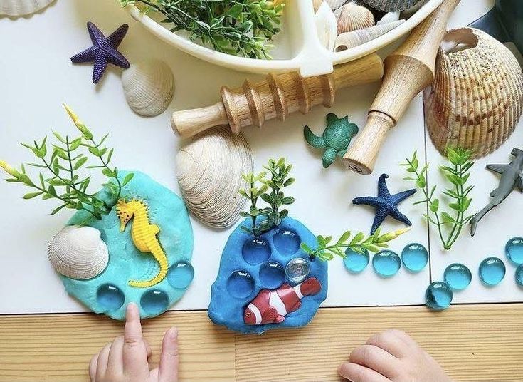 This may contain: a child's hand is pointing at some sea shells and plants on the table