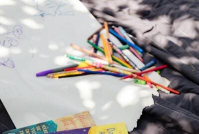colored pencils, paper and books on a blanket outside