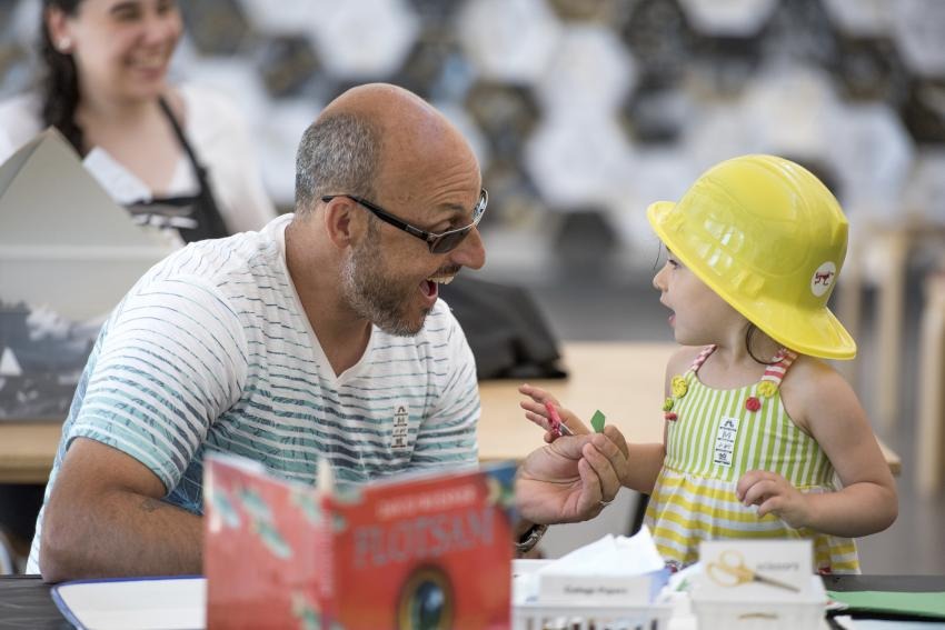 An adult and child joyfully making a collage together in the Art Studio.
